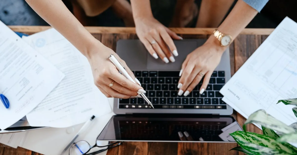 Deux collègues collaborant au bureau, travaillant sur un ordinateur portable avec des documents.