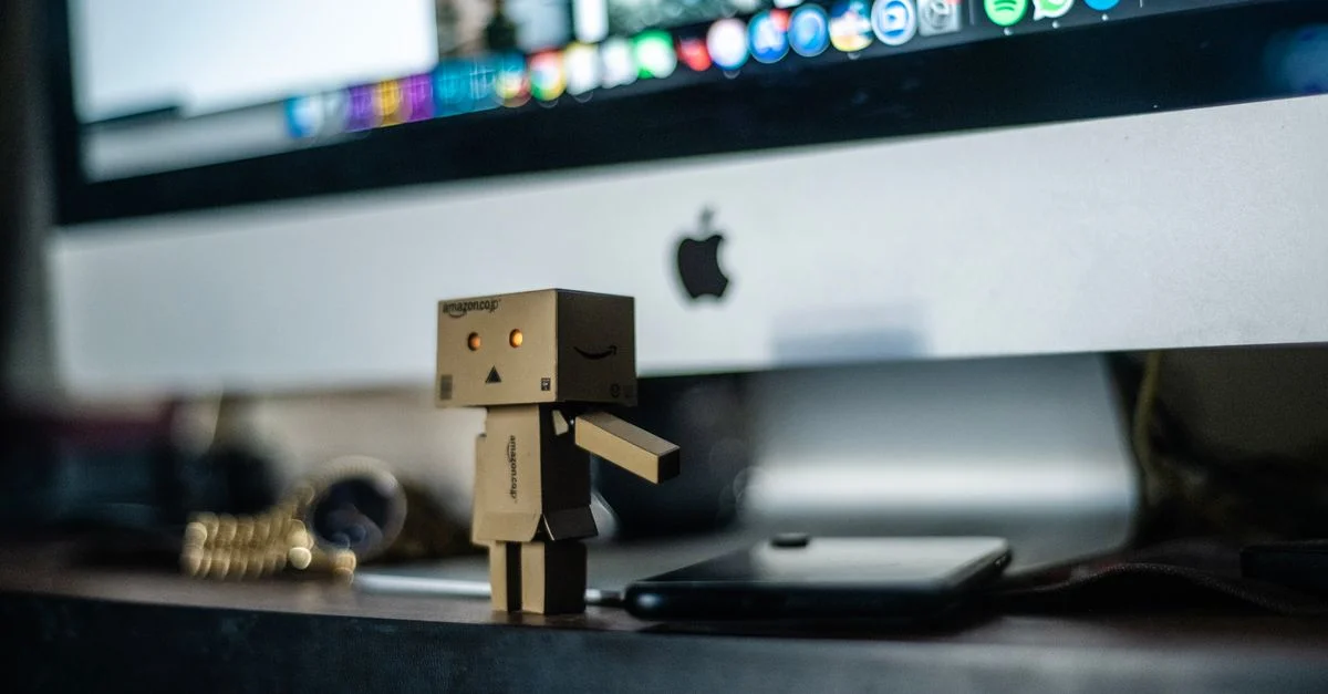 Un petit robot en carton exposé devant un écran d'ordinateur, ajoutant du charme à l'espace de travail.