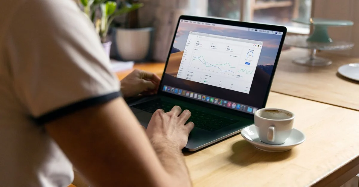 Personne travaillant sur un ordinateur portable avec des analyses dans un bureau à domicile confortable, café à la main.