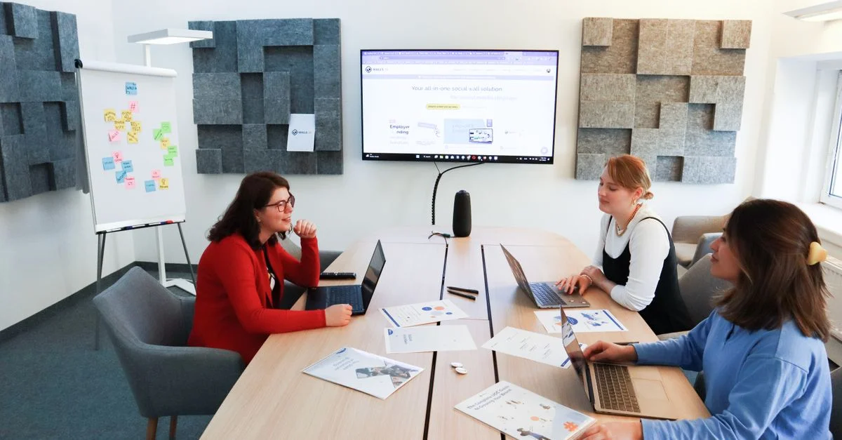 Trois femmes participant à une réunion d'affaires discutent d'idées avec des ordinateurs portables et des documents dans un bureau moderne.