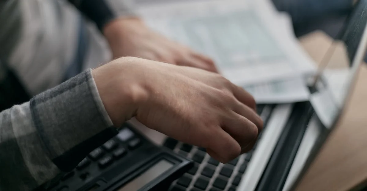 Gros plan sur des mains calculant des finances avec un ordinateur portable et des documents.